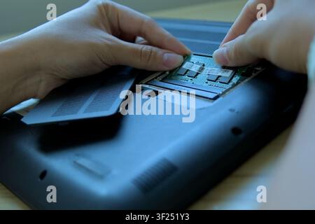 Detailed close-up of a technician's hands carefully aligning and installing a SO-DIMM RAM memory module into its slot inside an open laptop. Concept o Stock Photo