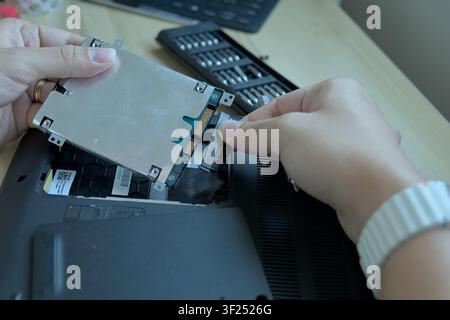 Close-up of hands disconnecting the flexible black SATA interface connector cable from a 2.5-inch laptop hard drive enclosure. Detail of internal comp Stock Photo