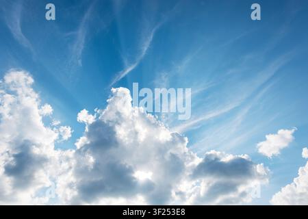 Dramatic blue sky over fluffy cumulus clouds, streaked with delicate cirrus. Prominent crepuscular rays create a divine, hopeful light effect. Ideal b Stock Photo