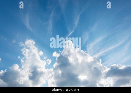 Spectacular sun rays shining through fluffy cumulus clouds under a bright blue sky with wispy cirrus. Inspiring and peaceful nature background perfect Stock Photo