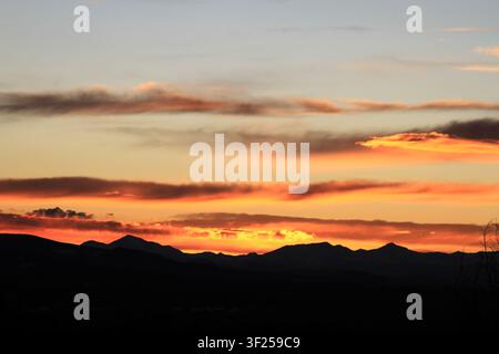 Brilliant orange and red sunset glows behind silhouetted mountain peaks in the Colorado Rockies. Stock Photo