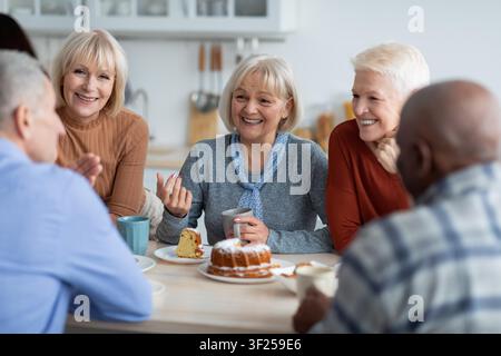 Happy Senior Women Enjoying Coffee And Cake Together At Modern Kitchen Table, Lifestyle Concept Stock Photo