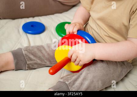 Two year old focusing on ring stacking playing with plastic pyramid toy. Logic and thinking skills growth. Bright colors attract attention. Fine motor Stock Photo