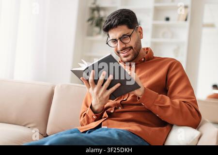 Focused Young Man Reading Book At Home, Relaxing On Couch, Wellness Concept Stock Photo