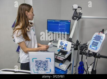 Kyiv, Ukraine - May 29, 2026: Young female medical technician with headphones operates advanced diagnostic equipment in a neurological laboratory. Hol Stock Photo