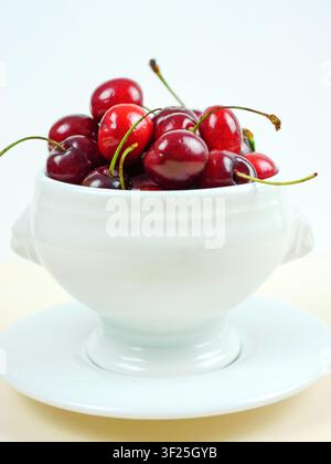 Minimalist macro shot of fresh red cherries in white bowl on white background Stock Photo