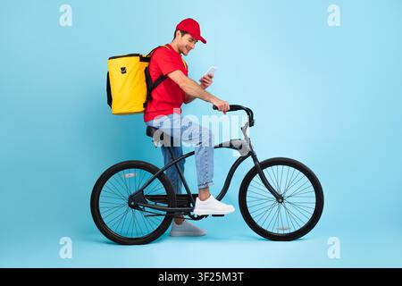 Happy Young Man Riding Bicycle With Delivery Bag, Using Smartphone, Weight Loss Concept Stock Photo