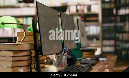 Desktop monitors with blue screen and AI chatbot in library workspace, data automation and abstract display background at desk. Wooden table with headphones and stack of books. Stock Photo