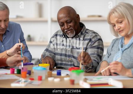 Smiling Black Male Senior Participating In Art Class, Focusing On Painting Activity Stock Photo