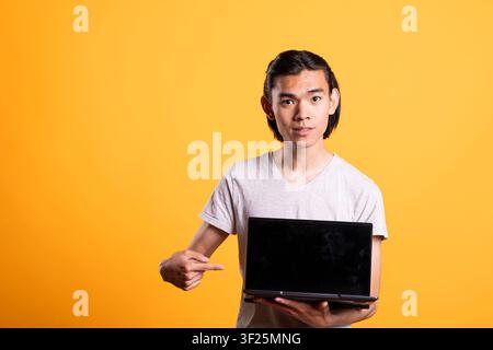 Person with laptop points at empty black screen, inviting space for advertising or branding. Confident man gesturing at device with mockup display, representing technology, apps and online business. Stock Photo
