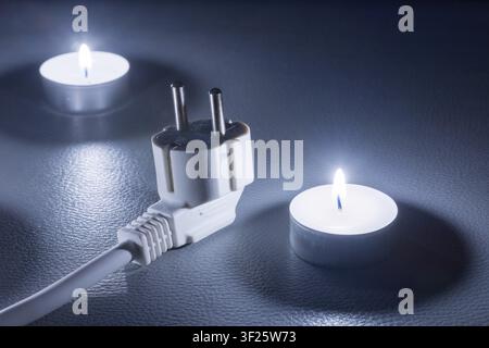 Two candles and an electric cable in cold light on a dark background, symbolic picture, power failure, blackout, plug Stock Photo