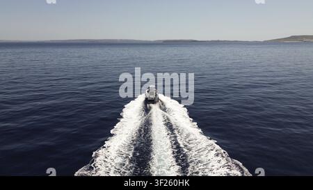 A lone boat sails across the calm blue ocean under a clear sky, leaving a white trail of waves behind. Heading to Malta Stock Photo