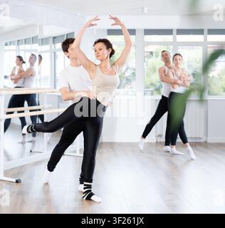 Diligent couple of athletic modern ballet dancers practicing ballet poses with support in hall with ballet bar Stock Photo