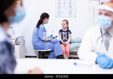 Nurse recording child data on clipboard in medical clinic while providing pediatric care, child data or symptom checking during a clinic visit. Stock Photo