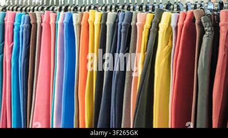 Colorful pants hang on clothing rack. Various bright hues fill the scene. Multiple vibrant colors are visible. retail clothing display Stock Photo