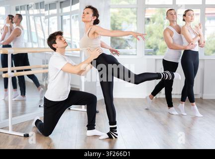 Diligent couple of athletic modern ballet dancers practicing ballet poses with support in hall with ballet bar Stock Photo