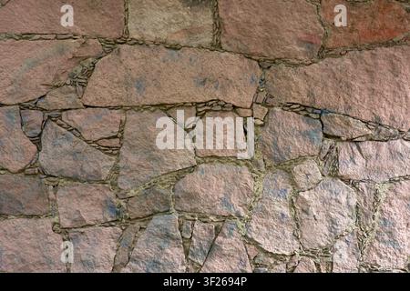 Rough stones form a weathered, ancient wall. Pinkish hues glow under natural light. Cracks and joints show time's passage. Texture invites tactile ima Stock Photo