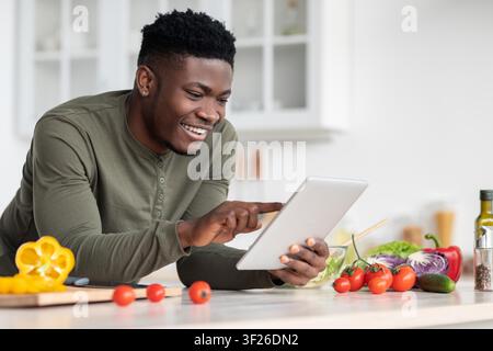 Smiling Black Male Chef Using Tablet In Modern Kitchen, Preparing Healthy Recipe Stock Photo