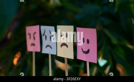 Four emotion sticky notes showing different facial expressions on natural green background, ideal for mental health, psychology, mood Stock Photo