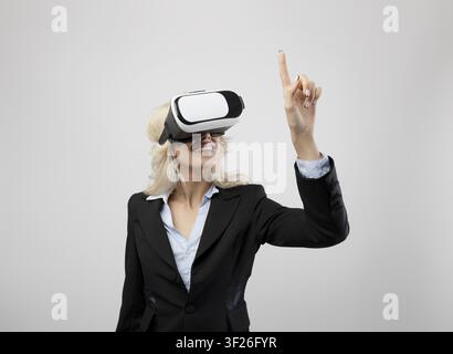 Smiling Young Caucasian Woman Wearing Vr Headset In Business Suit, Pointing At Virtual Interface, Office Stock Photo