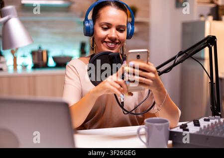 Influencer reads fan messages on a phone during a live social media show, supporting online broadcast, audience contact and creator content. Stock Photo