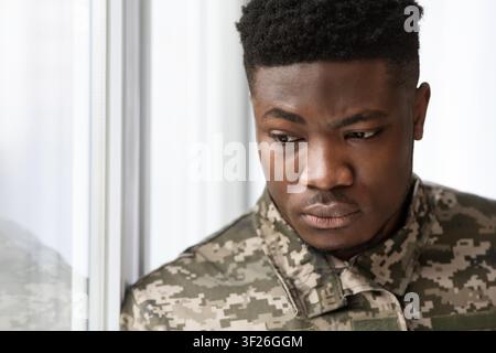 Serious Young Black Man In Military Uniform Looking Thoughtfully Out Window, Reflecting Stock Photo