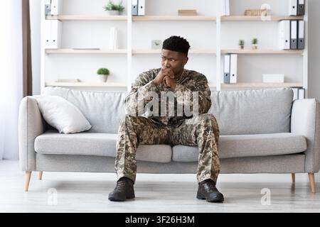 Pensive Young Black Man In Military Uniform Sitting At Home, Reflecting On Duty Stock Photo