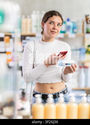 woman scans a mobile package with ointment against the background of shelves in a pharmacy Stock Photo
