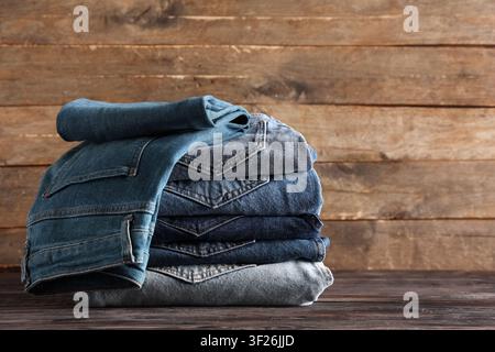 Stack of folded blue denim jeans in various washes on a dark wooden table with a rustic wood background Stock Photo