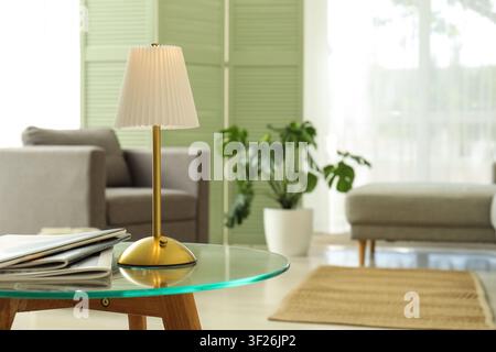 Modern living room interior with a stylish table lamp on a glass coffee table and blurred background, Newspapers and magazines are neatly stacked on t Stock Photo