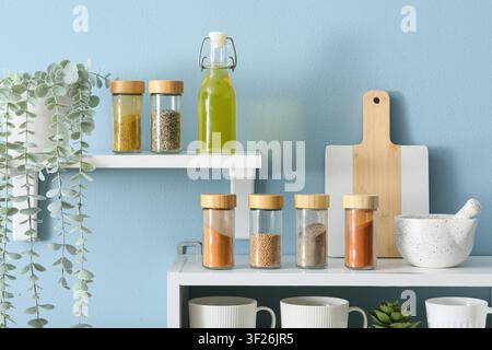 Kitchen shelves with various spices, cooking oil, and kitchenware against a light blue wall background Stock Photo