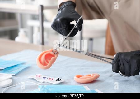 Piercer in black gloves practicing ear piercing on a silicone ear model with sterile tools and jewelry, the scene includes various piercing jewelry Stock Photo
