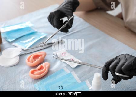 Piercing artist in black gloves holding sterile tools and jewelry for ear piercing procedure Stock Photo