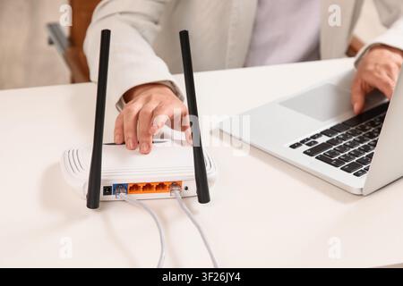 Person connecting ethernet cables to a white wireless router on a desk next to a laptop, internet connectivity Stock Photo