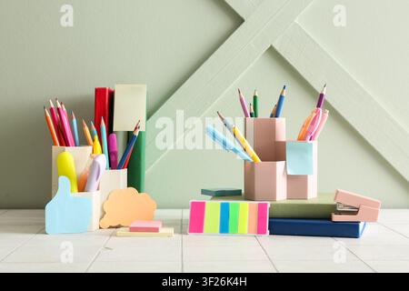 Colorful school and office supplies with pencils, pens, and sticky notes on a light green background Stock Photo