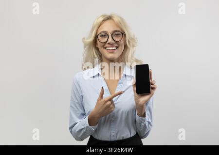 Smiling Young Caucasian Woman Pointing At Smartphone In Office, Business Concept Stock Photo