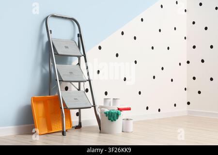 Home renovation with painting tools, step ladder, paint cans, and roller tray in a room with polka dot wall Stock Photo