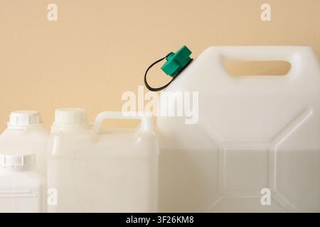 White plastic jerry cans and bottles with a green cap against a beige background, industrial packaging and storage Stock Photo