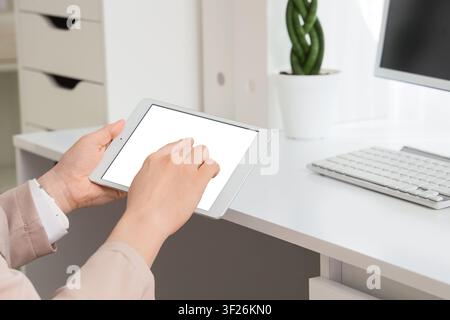 Person holding a white digital tablet with a blank screen, interacting with a finger tap in a modern office setting Stock Photo