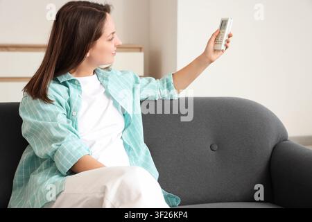 Young woman adjusting air conditioner temperature with remote control while relaxing on a sofa at home Stock Photo