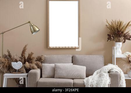 Vertical wooden frame mockup on a beige wall above a neutral sofa with decorative elements, a neutral-toned sofa with textured pillows and a cozy thro Stock Photo