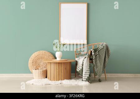 Empty picture frame on a mint green wall with a rattan chair, wooden table, and decorative elements in a cozy room Stock Photo