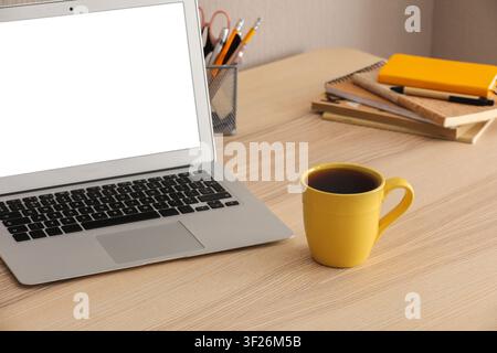 Laptop with blank white screen and yellow coffee mug on a light wooden desk, home office or remote work setup Stock Photo