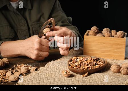 Woman cracking walnuts with nutcracker on wooden table Stock Photo