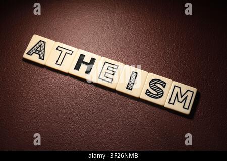 Atheism word spelled out with letter tiles on a dark brown textured background belief systems and philosophy, this arrangement concepts of belief syst Stock Photo
