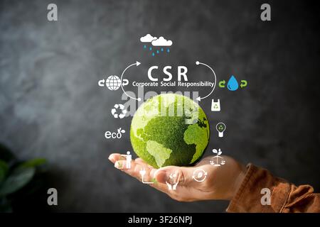 A hand presents a green globe surrounded by CSR and eco icons, representing corporate social responsibility, recycling, water conservation, ethical bu Stock Photo