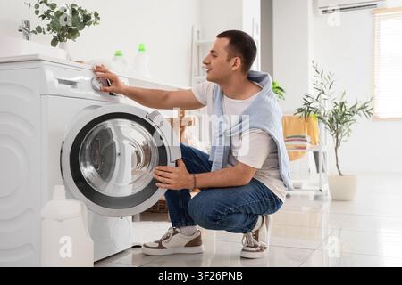 Young man using washing machine in laundry room Stock Photo