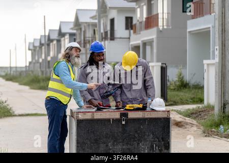 Senior Engineers discussing blueprint at housing construction site during daytime, concept of teamwork and residential project management, Real estate Stock Photo