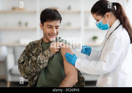 Smiling Young Caucasian Man Getting Vaccinated In Clinic By Female Healthcare Professional Stock Photo