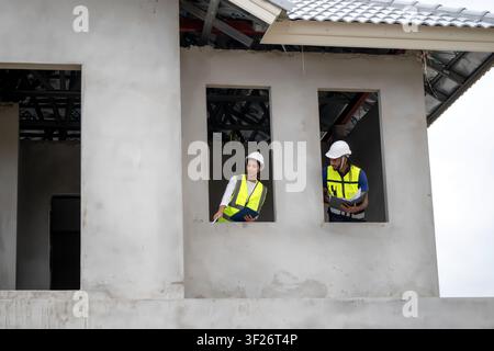Construction managers inspecting unfinished house structure from second floor window layout during daytime, concept of teamwork and professional build Stock Photo
